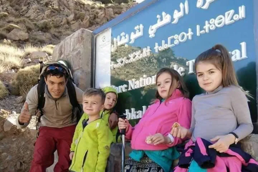 Trekkers of all ages at the Toubkal National Park sign on a day walk above Imlil.